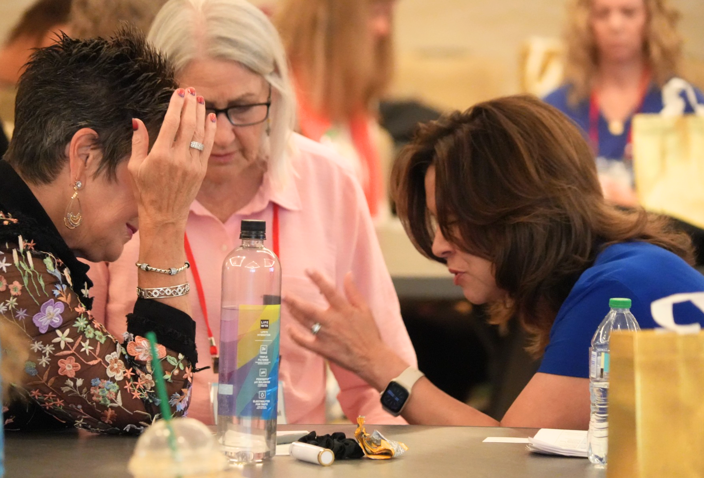 Three women praying together at a table during the conference
